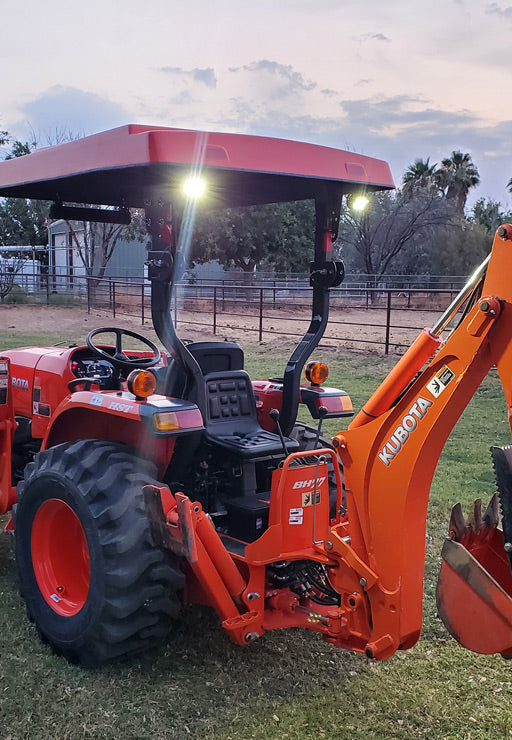 Kubota compact tractor and backhoe equipped with an orange Tractor Sunshade R-Series canopy and two rear-mounted work lights.