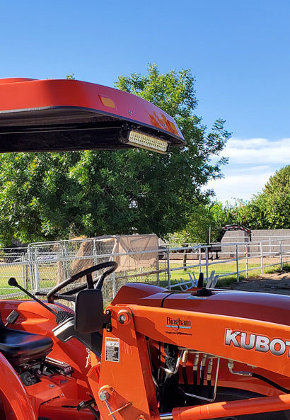 Orange Kubota tractor equipped with a matching Tractor Sunshade R-Series canopy and an LED light bar mounted beneath the front edge.