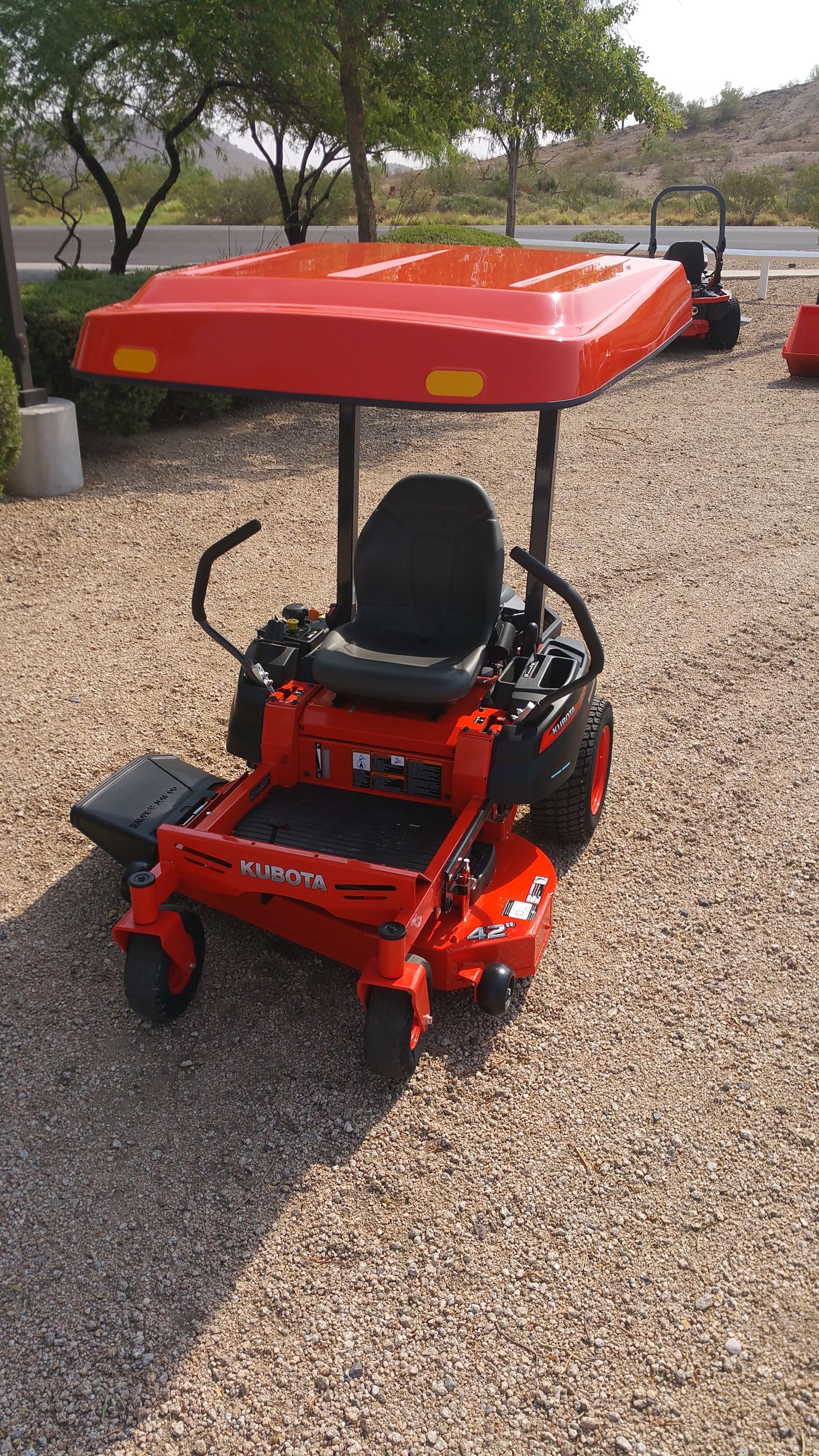 Front view of a Kubota zero-turn mower equipped with an orange Tractor Sunshade R-Series canopy on a gravel work area.