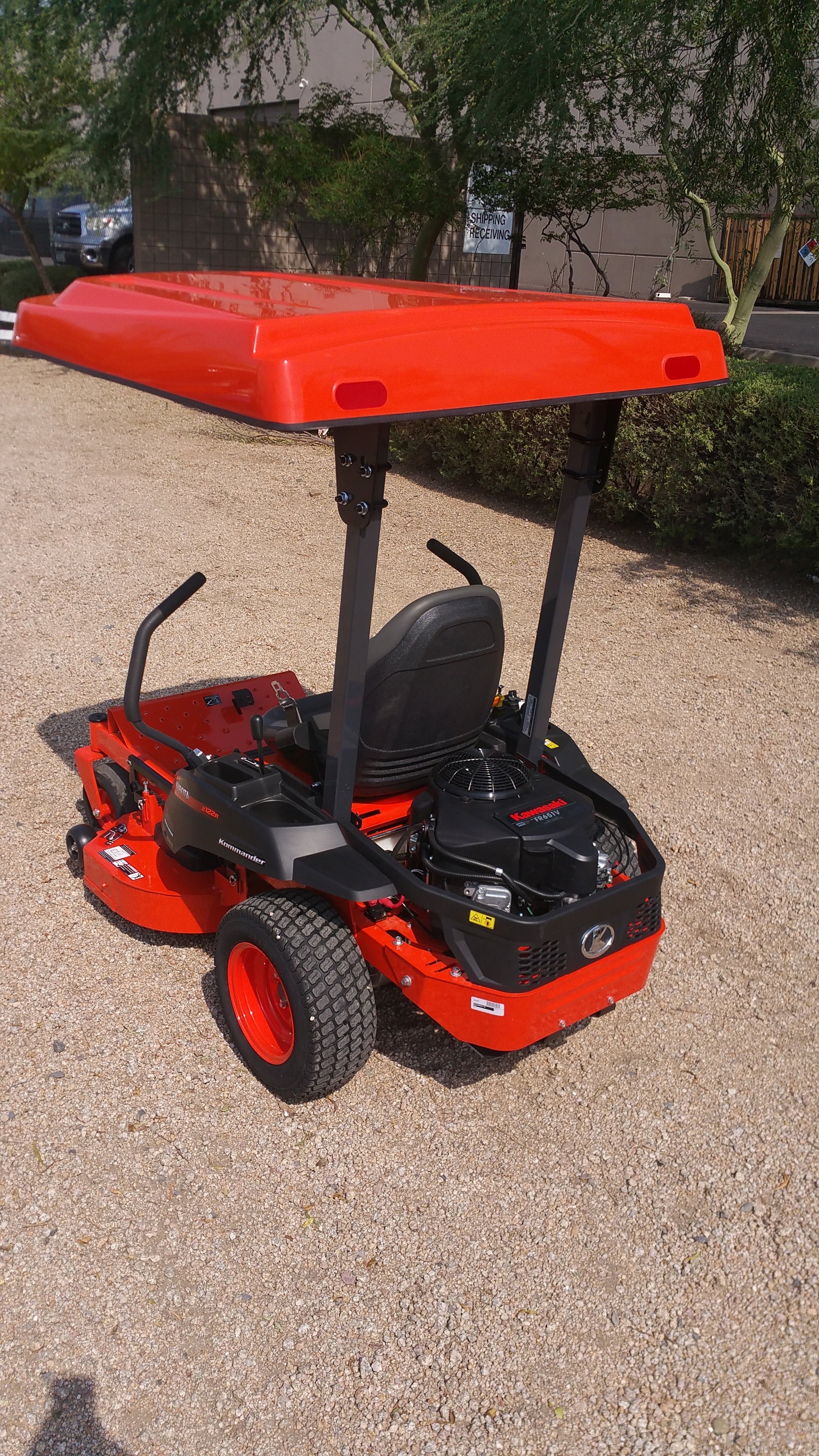 Rear three-quarter view of a Kubota zero-turn mower equipped with an orange Tractor Sunshade R-Series canopy and dual mounting posts.
